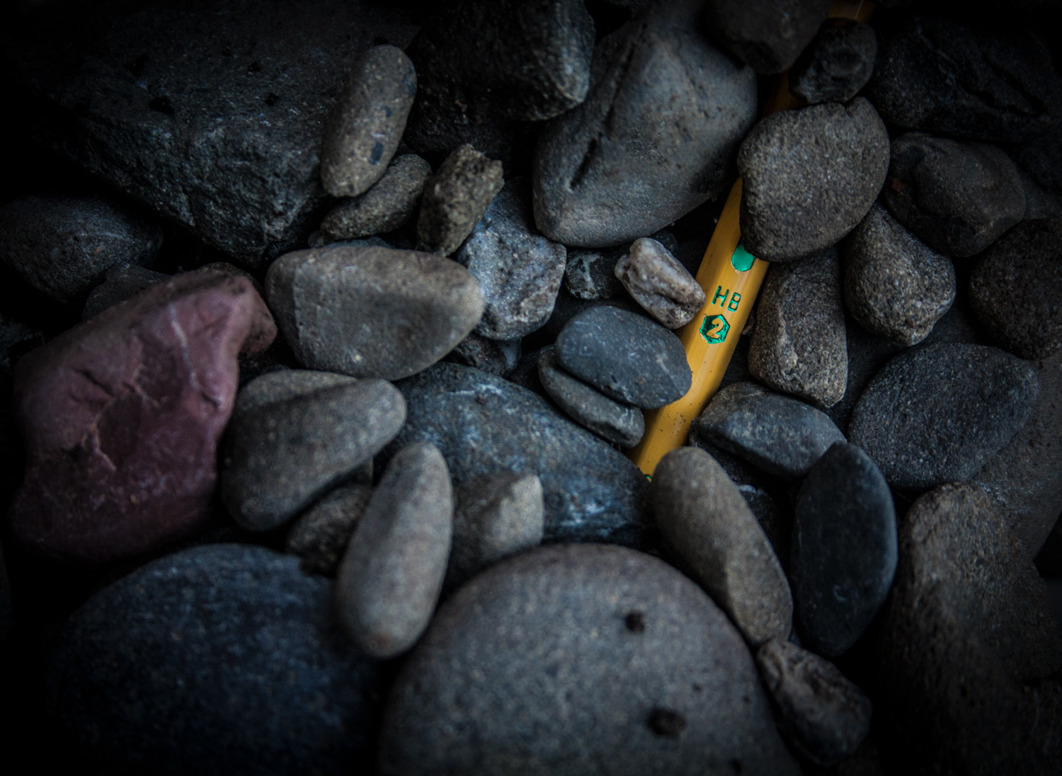 A photo of gray rocks covering a number two pencil.